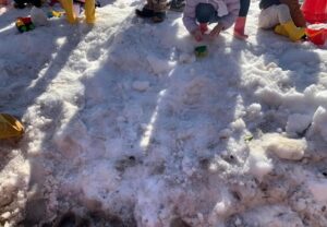 地面の雪を手にとって遊ぶ子どもたち